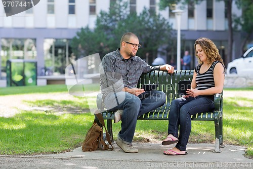 Image of Students With Digital Tablets Sitting On Bench At Campus