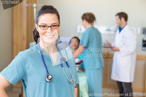 Image of Nurse Smiling Against Patient And Medical Team In Hospital