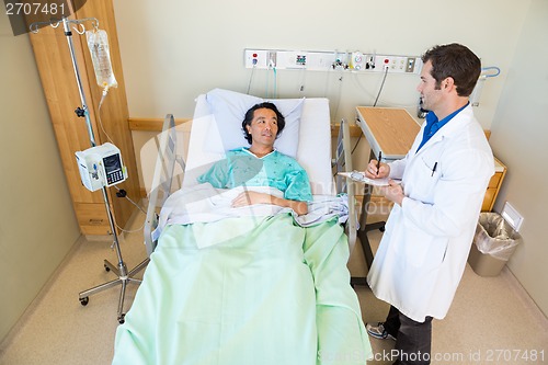 Image of Male Doctor Looking At Patient While Writing Notes On Clipboard