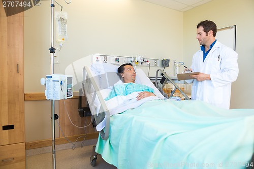 Image of Doctor Looking At Patient While Writing Notes On Clipboard