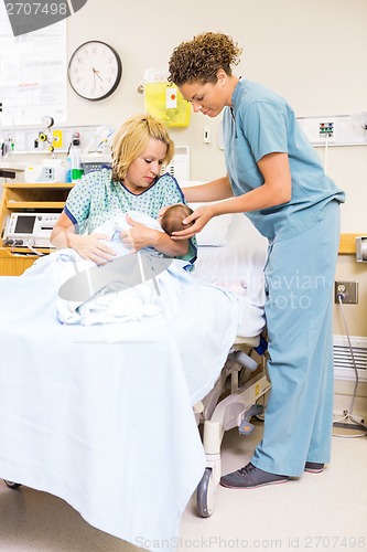 Image of Nurse Assisting Woman In Holding Newborn Baby At Hospital