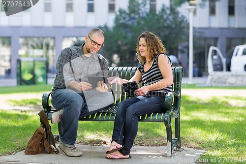 Image of Students Using Digital Tablet On Bench At Campus