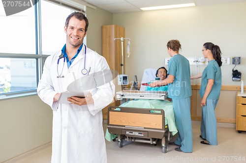 Image of Doctor Using Tablet Computer With Nurses And Patient In Backgrou