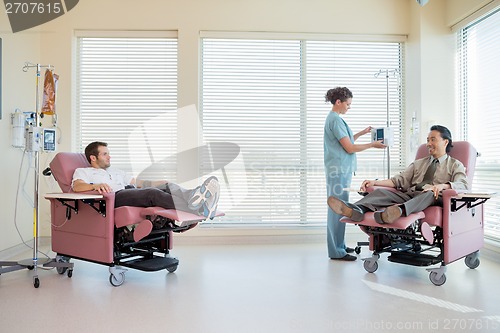 Image of Nurse Adjusting IV Machine While Patients Reclining On Chair