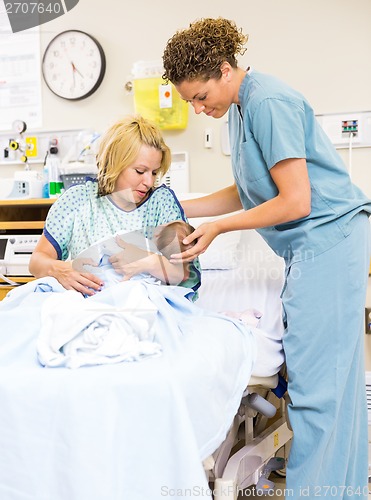 Image of Nurse Helping Woman In Holding Newborn Baby At Hospital