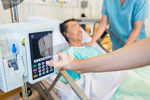 Image of Nurse's Hand Operating IV Machine While Patient In Background
