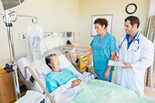 Image of IV Bag On Rod With Medical Team Looking At Patient