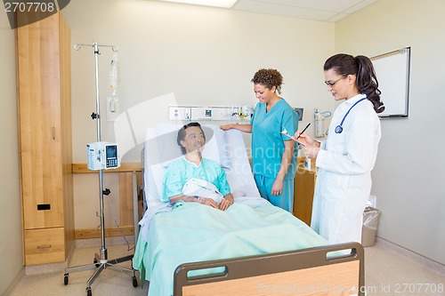 Image of Patient Looking At Doctor Writing Notes While Nurse Standing By