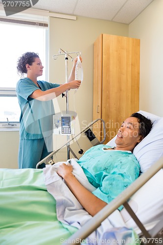 Image of Nurse Adjusting IV Drip On Rod With Patient On Foreground