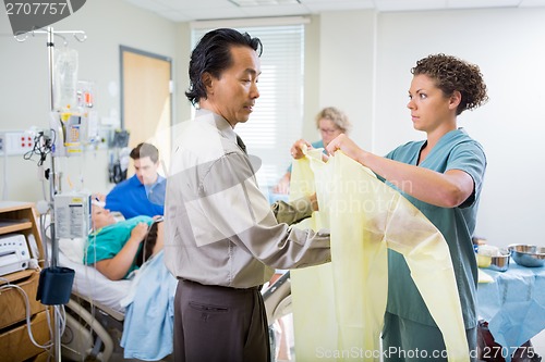 Image of Nurse Assisting Doctor In Wearing Operation Gown At Hospital