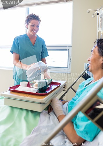 Image of Nurse Lifting Cover From Food Plate For Patient In Hospital