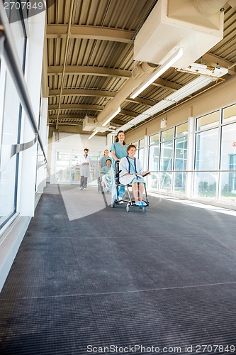 Image of Female Nurses Pushing Patients On Wheelchairs At Hospital Corrid