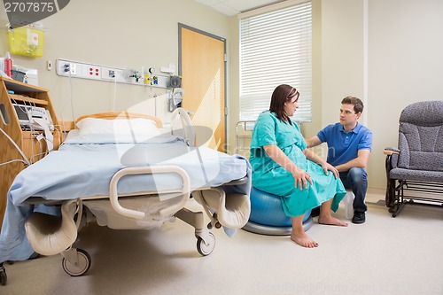 Image of Man Looking At Pregnant Wife On Exercise Ball In Hospital