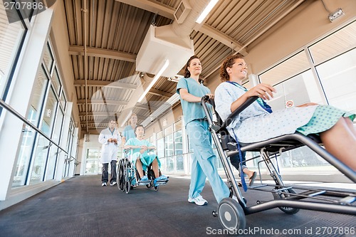 Image of Nurses Pushing Patients On Wheelchairs With Doctor At Corridor
