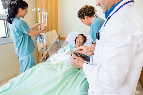 Image of Doctor Using Digital Tablet With Nurses Examining Patient In Hos