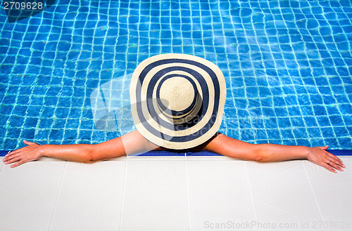 Image of Woman in straw hat relaxing swimming pool