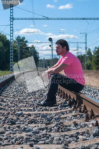 Image of One man in pink t-shirt sitting on train tracks