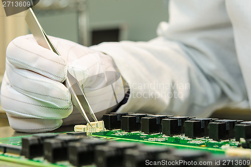 Image of Female hand holding tweezers and installing connector on PCB