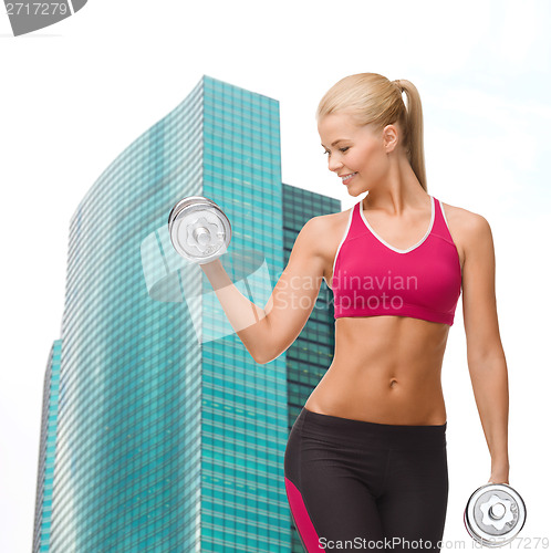 Image of smiling woman lifting steel dumbbell