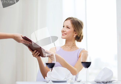 Image of smiling woman giving menu to waiter at restaurant