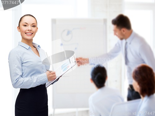 Image of young smiling businesswoman with clipboard and pen