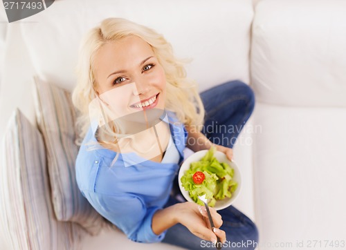 Image of smiling young woman with green salad at home
