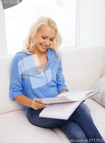 Image of smiling woman reading book and sitting on couch