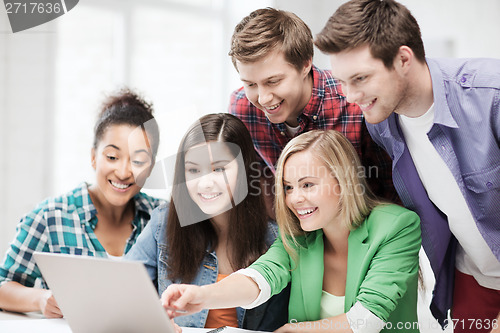 Image of smiling students looking at laptop at school