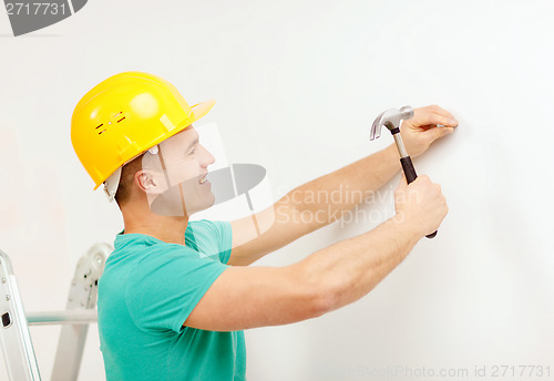 Image of smiling man in helmet hammering nail in wall