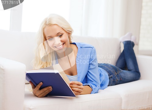 Image of smiling woman reading book and lying on couch