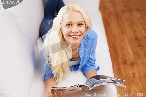 Image of woman lying on couch and reading magazine at home