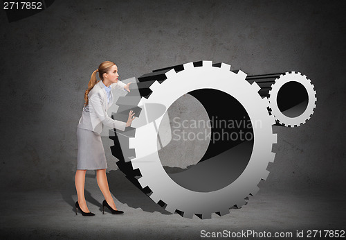 Image of busy businesswoman pushing cogwheel