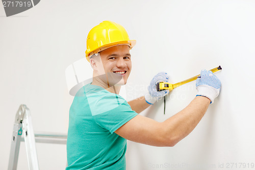 Image of smiling man in protective helmet measuring wall