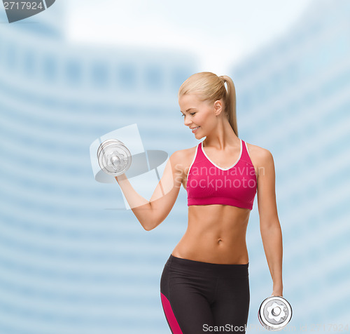 Image of smiling woman lifting steel dumbbell