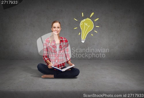 Image of smiling young woman sittin on floor with book