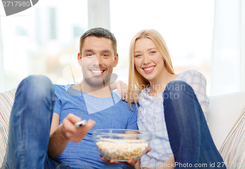 Image of smiling couple with popcorn watching movie at home