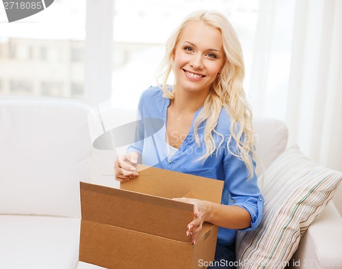 Image of smiling young woman opening cardboard box at home