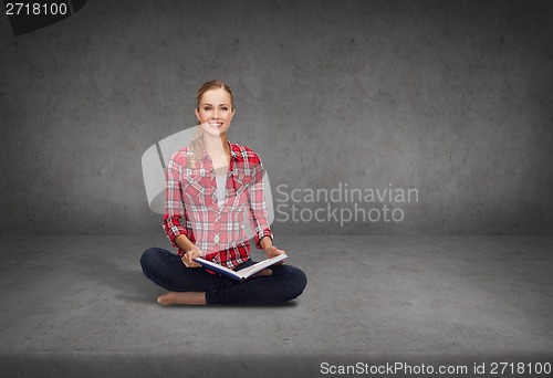 Image of smiling young woman sittin on floor with book