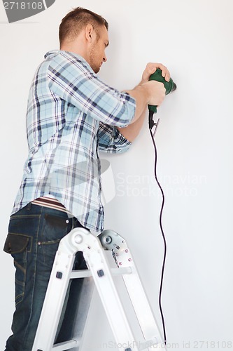 Image of man with electric drill making hole in wall