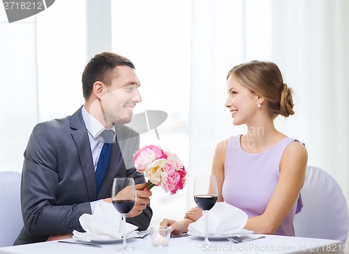 Image of smiling man giving flower bouquet at restaurant