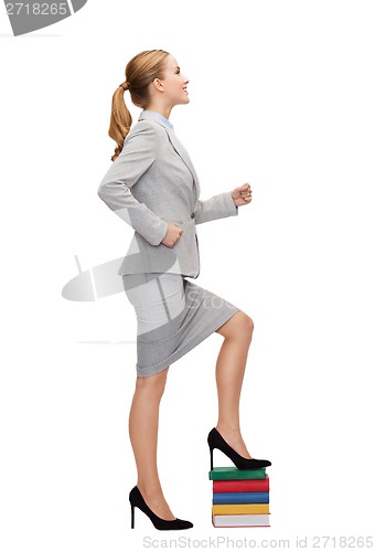 Image of smiling businesswoman stepping on pile of books