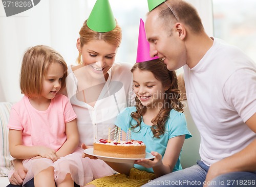 Image of smiling family with two kids in hats with cake