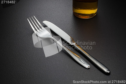 Image of bottle of beer, knife and fork on black