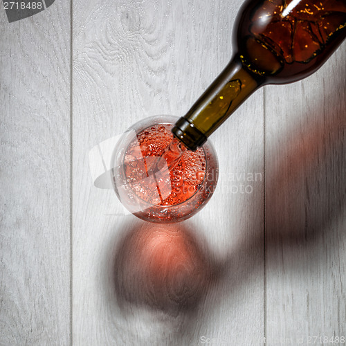Image of Red wine pouring into glass from bottle on white wooden table. T