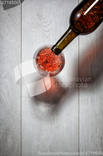 Image of Red wine pouring into glass from bottle on white wooden table. T