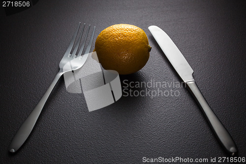 Image of lemon with knife and fork on black