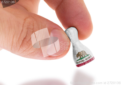 Image of Hand holding wooden pawn, flag painting, selective focus