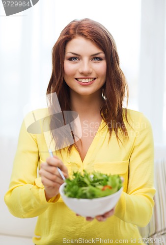 Image of smiling young woman with green salad at home