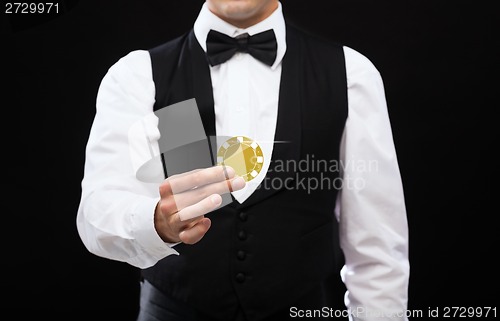 Image of dealer holding golden poker chip