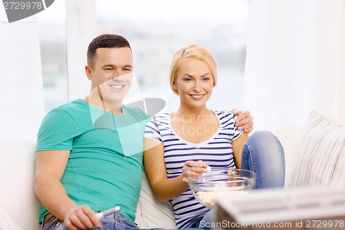 Image of smiling couple with popcorn watching movie at home